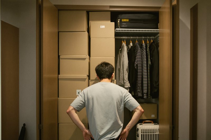 箱でいっぱいの押し入れの前に立つ男性